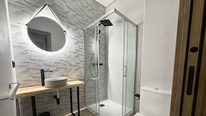 Uma casa de banho moderna com um espelho redondo, uma pia, uma sanita e uma cabine de duche em vidro.