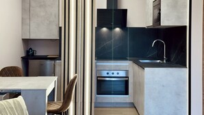 A modern kitchen with a built-in oven, a sink, and a dining area with a table and chairs. - Flower Deluxe - Garden Apartment-6082B (Noja)