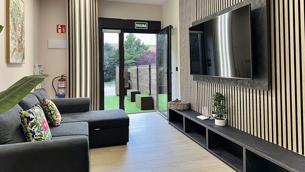 Un soggiorno moderno con un divano, una televisione a schermo piatto e una porta scorrevole in vetro che si apre su un giardino.