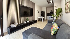 Un soggiorno moderno con una TV a schermo piatto, divani grigi, un'area pranzo e una cucina sullo sfondo.