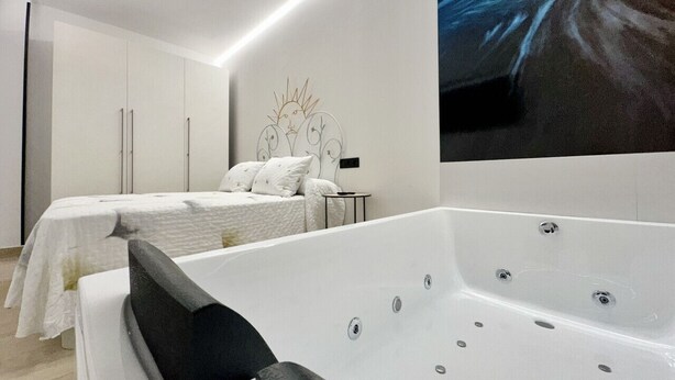 Ein modernes Schlafzimmer mit einer großen weißen Badewanne, einem Doppelbett mit weißer Bettwäsche und einem minimalistischen Design.