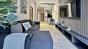 Ein modernes Wohnzimmer mit einem grauen Sofa, einem großen Fernseher und einem Holzboden.