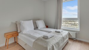 A bedroom with a bed, a nightstand, a window with a view, and a radiator. - Horizon 169 - SeaView by GrandApartments (Gdansk)