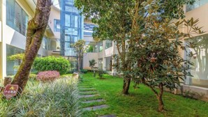 Un patio con sendero de piedra, abundante vegetación y un edificio con grandes ventanales y balcones.