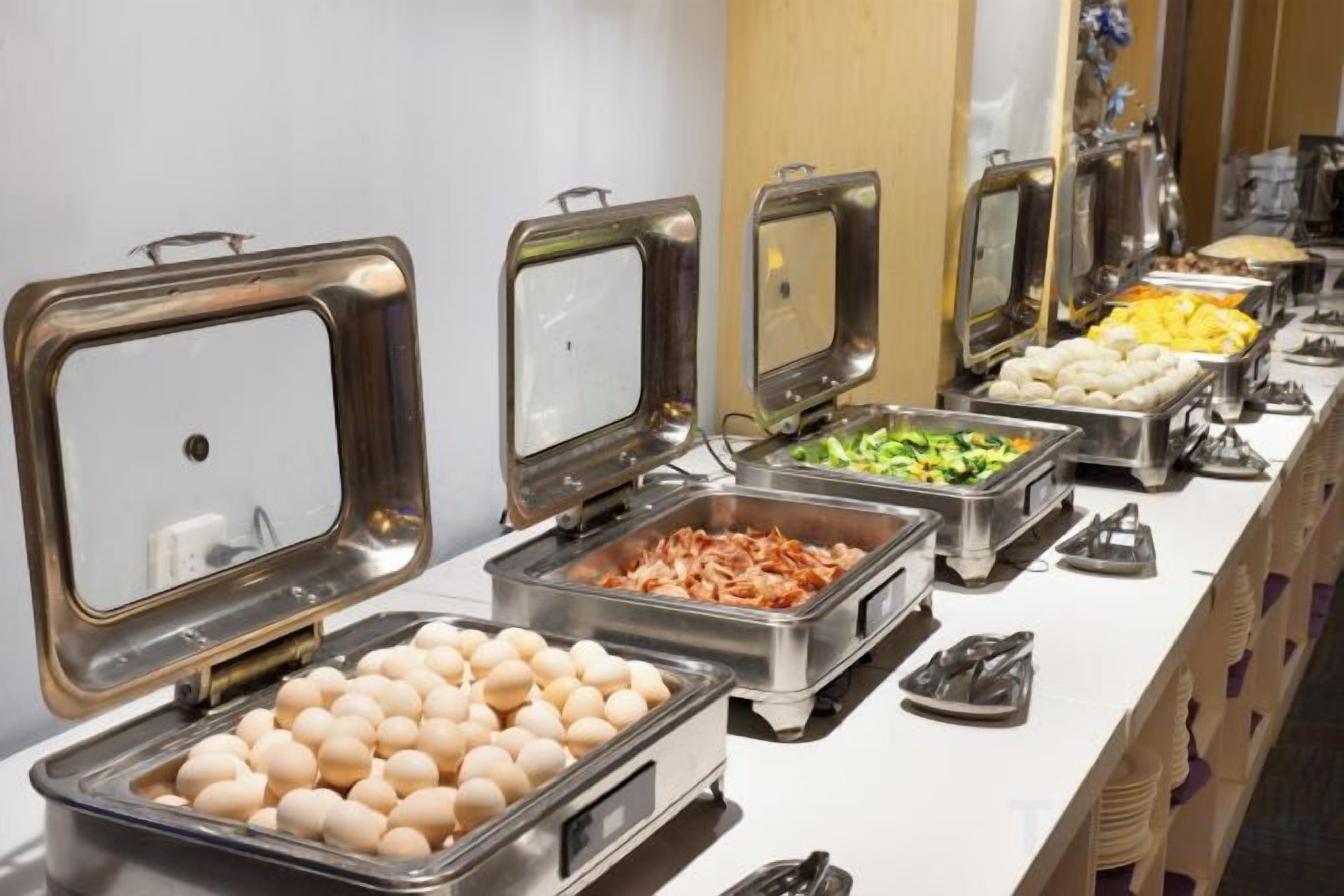 Un bufé con distintos alimentos en recipientes metálicos.