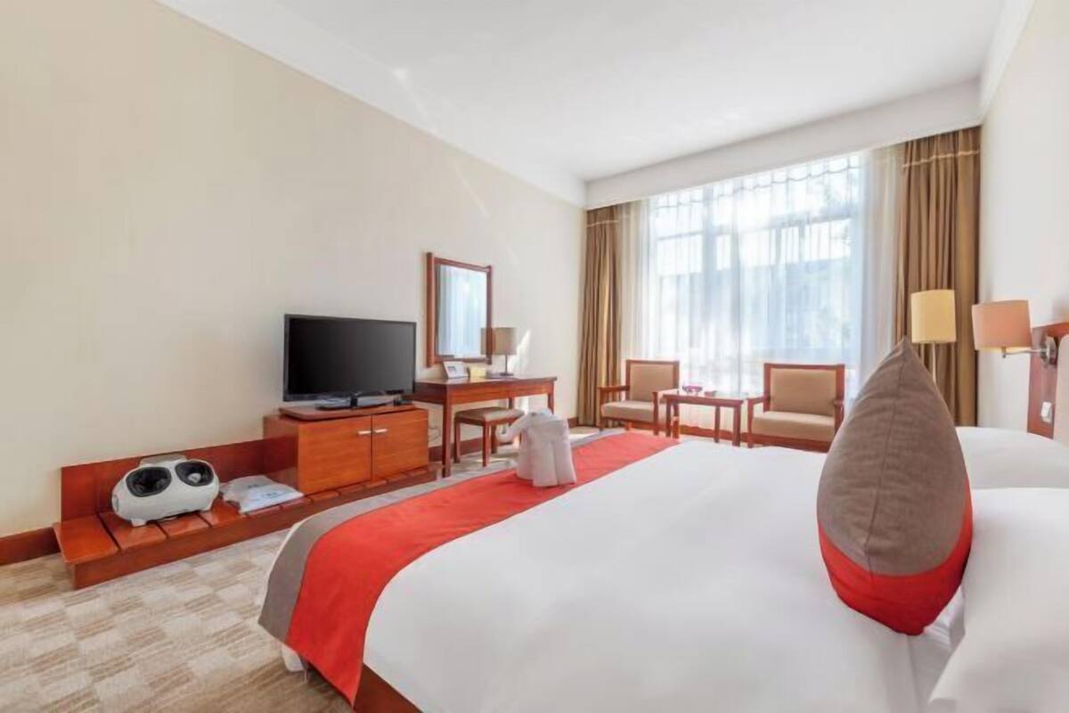 Een hotelkamer met een groot bed, een televisie, een bureau, een stoel en een raam met gordijnen.