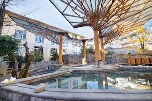 Un área de piscina con estructura de techo de cristal, escalones de piedra y el reflejo de edificios.