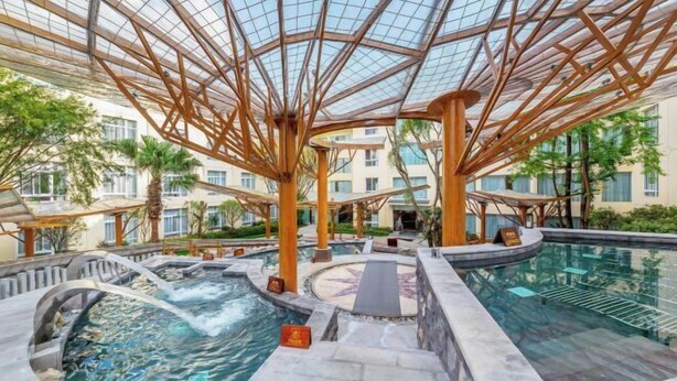 Un hotel con piscina infinita envuelta en cristal, varias tinas de hidromasaje y un diseño arquitectónico moderno con vigas y columnas de madera.