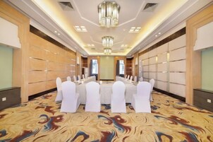 Un salón de conferencias con una larga mesa, sillas blancas y una alfombra estampada.