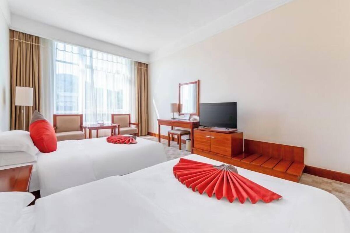 Een hotelkamer met twee bedden, een bureau, een televisietoestel en een raam met gordijnen.
