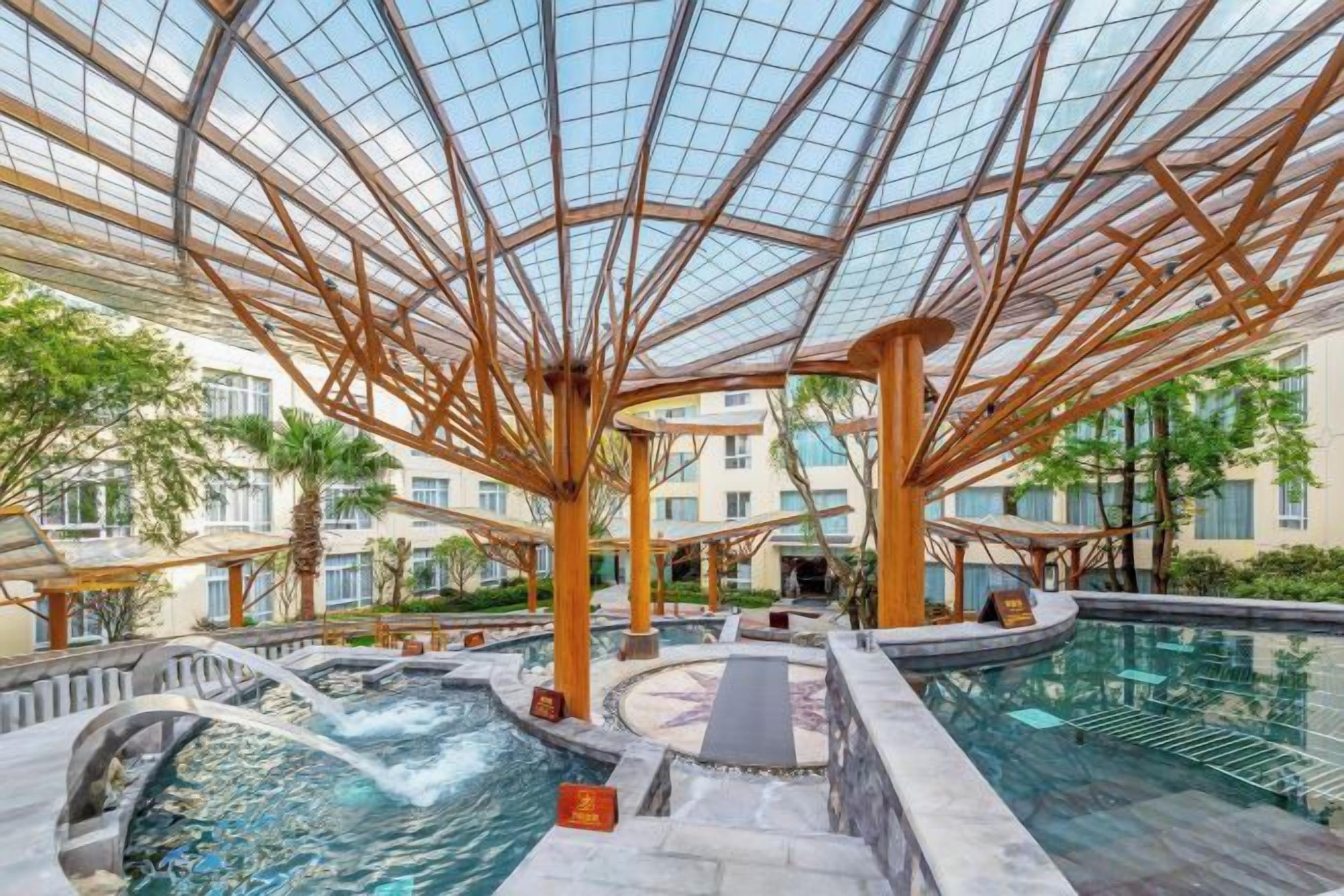 A hotel atrium with a glass ceiling, a central pool, and multiple balconies.