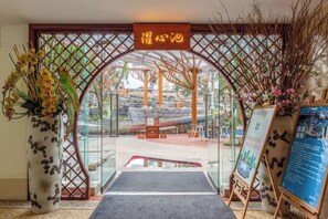 An entrance with a glass door, a sign above, a mat, a vase with flowers, and a signboard. - Tengchong Airport Sightseeing Hotel (Tengchong)