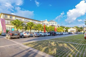 Un hôtel doté d’un parking, de plusieurs voitures et de palmiers.