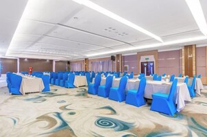 Un salón de banquetes con filas de mesas y sillas, una alfombra estampada y un diseño de techo moderno.