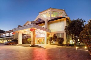 Un hotel moderno con entrada cubierta, zona de estacionamiento para coches y fachada bien iluminada.