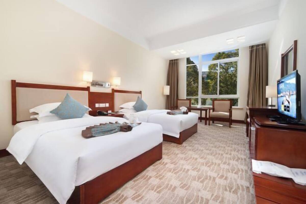 Een hotelkamer met twee bedden, een bureau, een televisie en een raam met gordijnen.