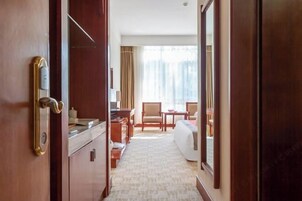 Habitación de hotel con puerta de madera, un escritorio, una silla, una cama y vistas al exterior a través de amplios ventanales.
