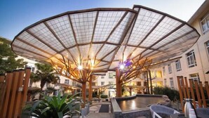 Un patio al aire libre con una amplia estructura de toldo semitransparente, arreglos de asientos y una fuente de agua.