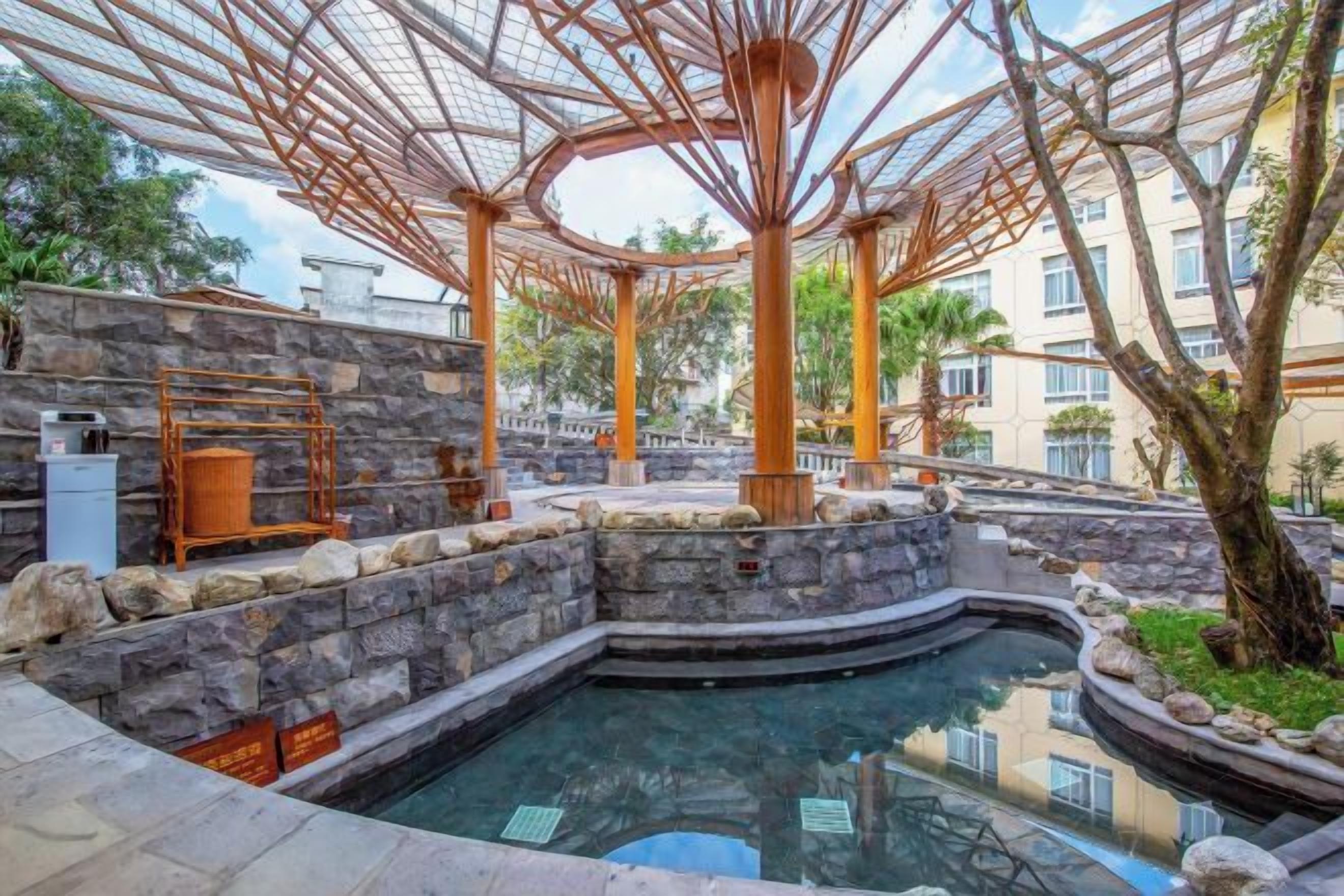 Un área de piscina con muro de piedra, pérgola de madera y un jacuzzi.