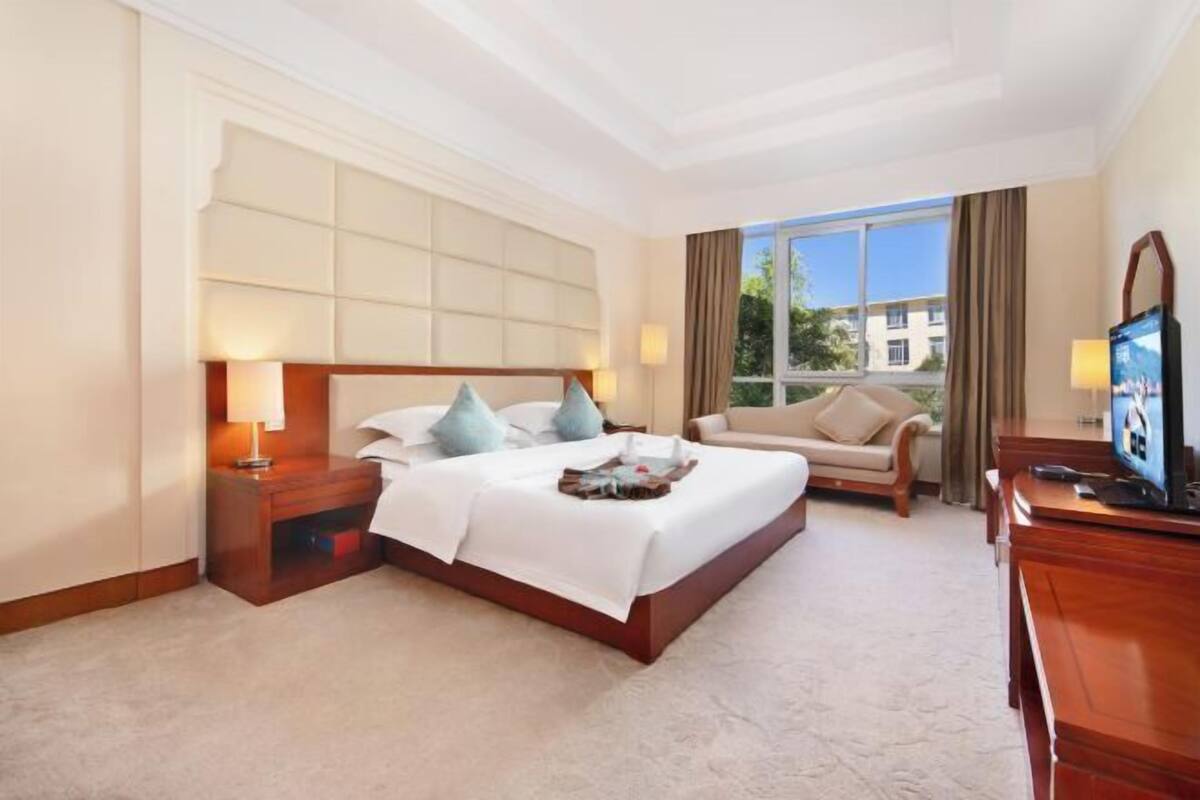 Een hotelkamer met een groot bed, een sofa, een televisie en een raam met uitzicht op gebouwen.