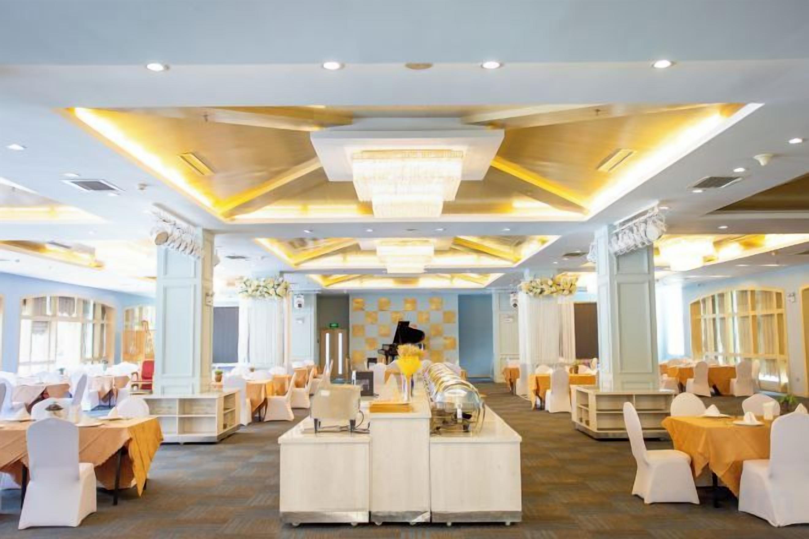 A banquet hall with round tables, a central bar area, and a chandelier.