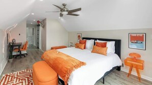 Une chambre à coucher avec un lit, un ventilateur de plafond, un bureau avec une chaise et une affiche accrochée au mur.