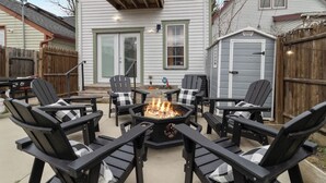 Un jardin avec un foyer entouré de fauteuils Adirondack, une terrasse en bois et un abri de jardin.