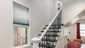 Un escalier moderne aux couleurs blanc et noir, menant à un palier agrémenté d’un rideau rouge et d’une fenêtre.