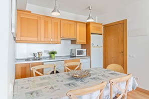 Een kleine keuken met houten kastjes, een magnetron, een vaatwasser en een eettafel met stoelen.