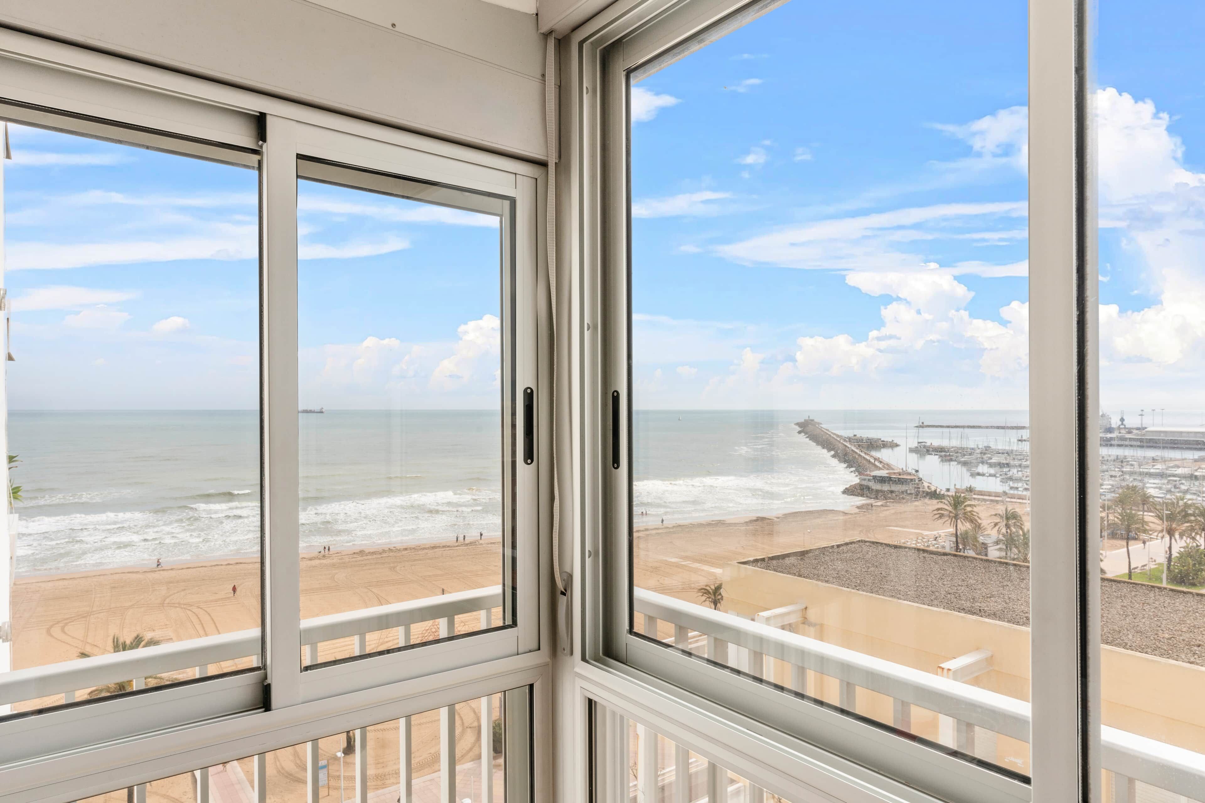 A view from a window overlooking a beach with a pier and boats.