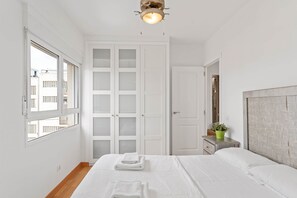 A bedroom with a bed, a wardrobe, a nightstand, a potted plant, and a window. - Apartment with Ocean View (Platja de Gandia)