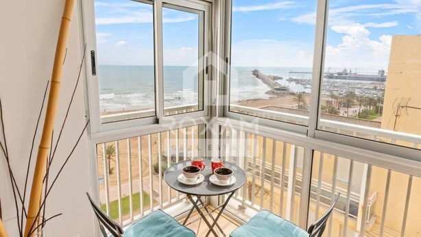 A balcony with a view of the ocean and a pier. There is a small table with two cups and saucers. - Ocean View Apartment (Platja de Gandia)