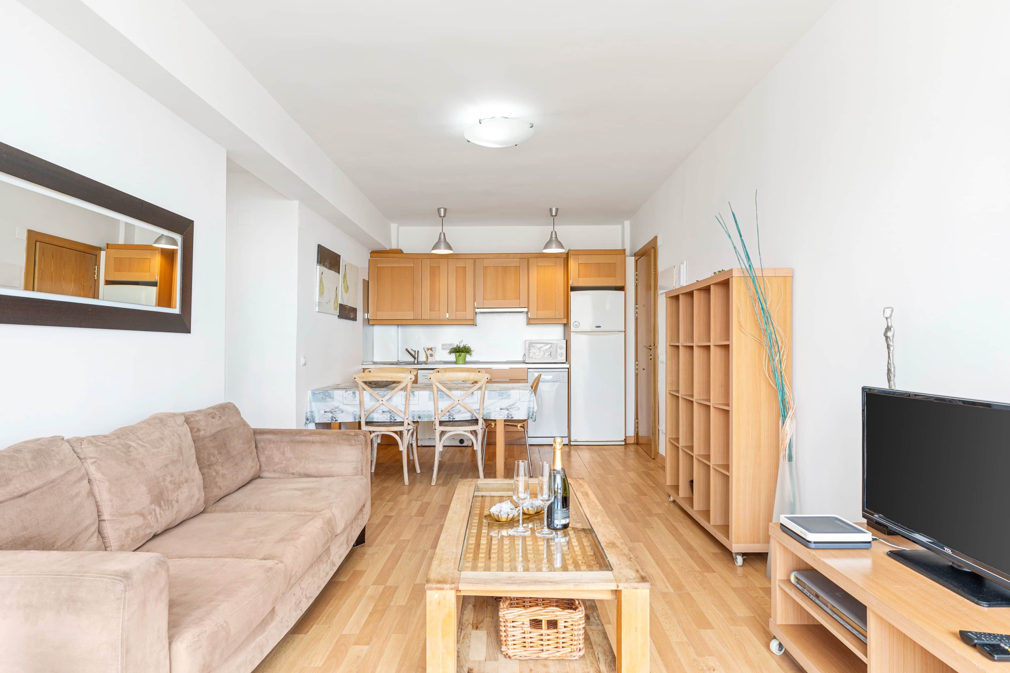 A compact living space with a sofa, a coffee table, a television, and a kitchen area with wooden cabinets and a microwave.