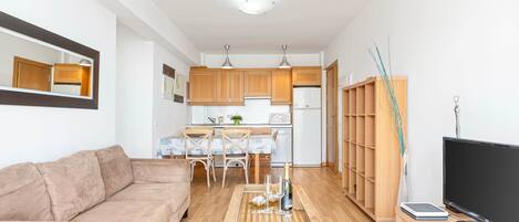 A compact living space with a sofa, a coffee table, a television, and a kitchen area with wooden cabinets and a microwave.
