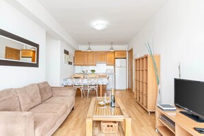 Een knus woongedeelte met een bank, salontafel, televisie en een keukenhoek met houten kastjes en een magnetron.