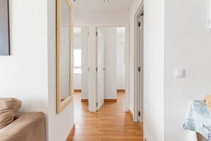 Um corredor com piso de madeira, paredes brancas e um sofá bege.