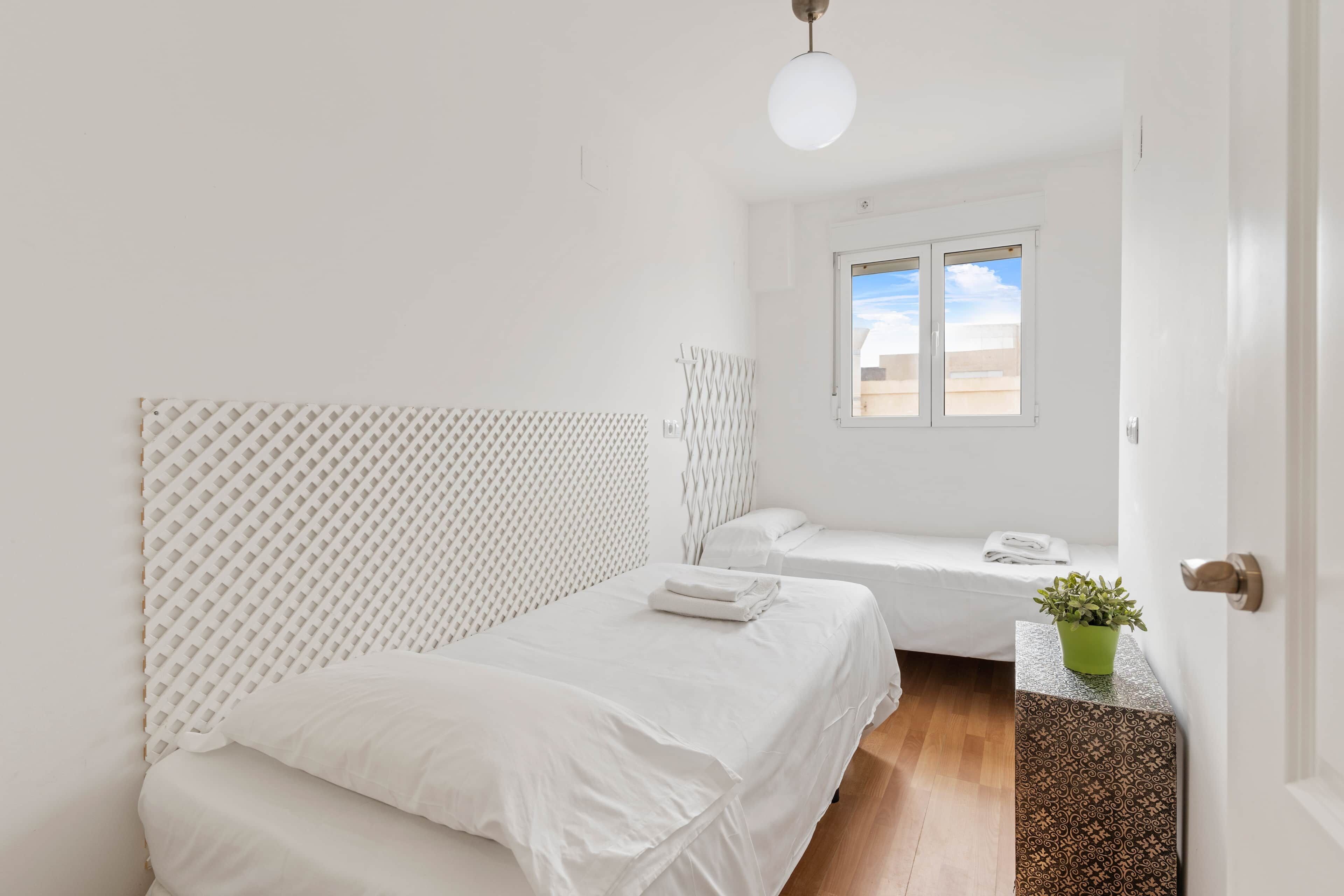 Un dormitorio minimalista con dos camas, una ventana con vistas y una planta en maceta.
