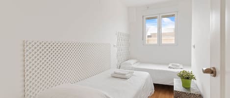 A minimalist bedroom with two beds, a window with a view, and a potted plant.