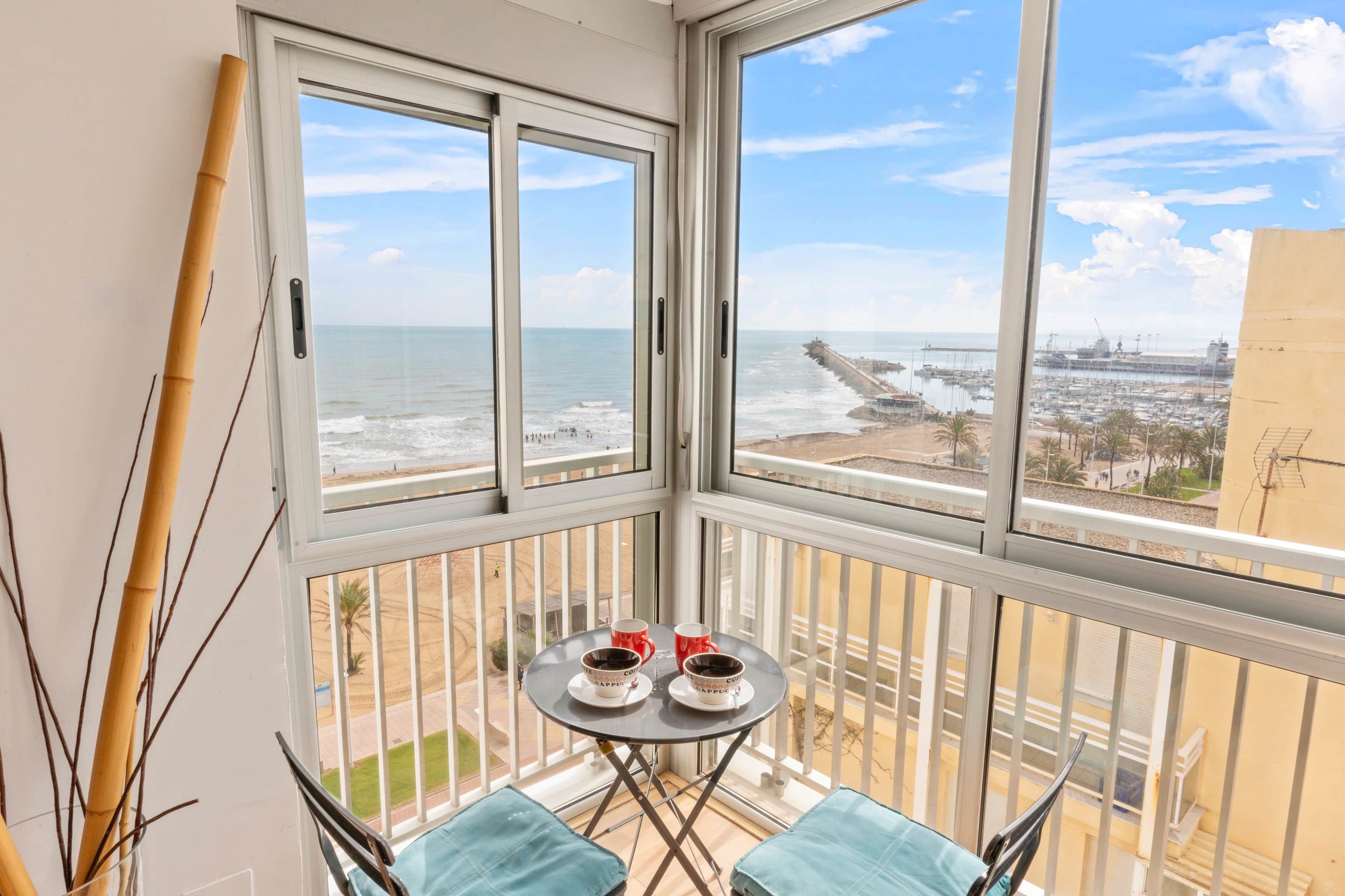 A balcony with a view of the sea and a marina. There is a small table with two cups and a saucer.