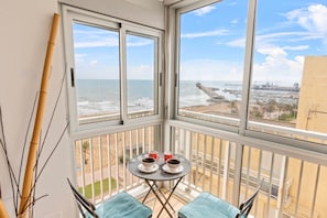 A balcony with a view of the sea and a marina. There is a small table with two cups and a saucer.