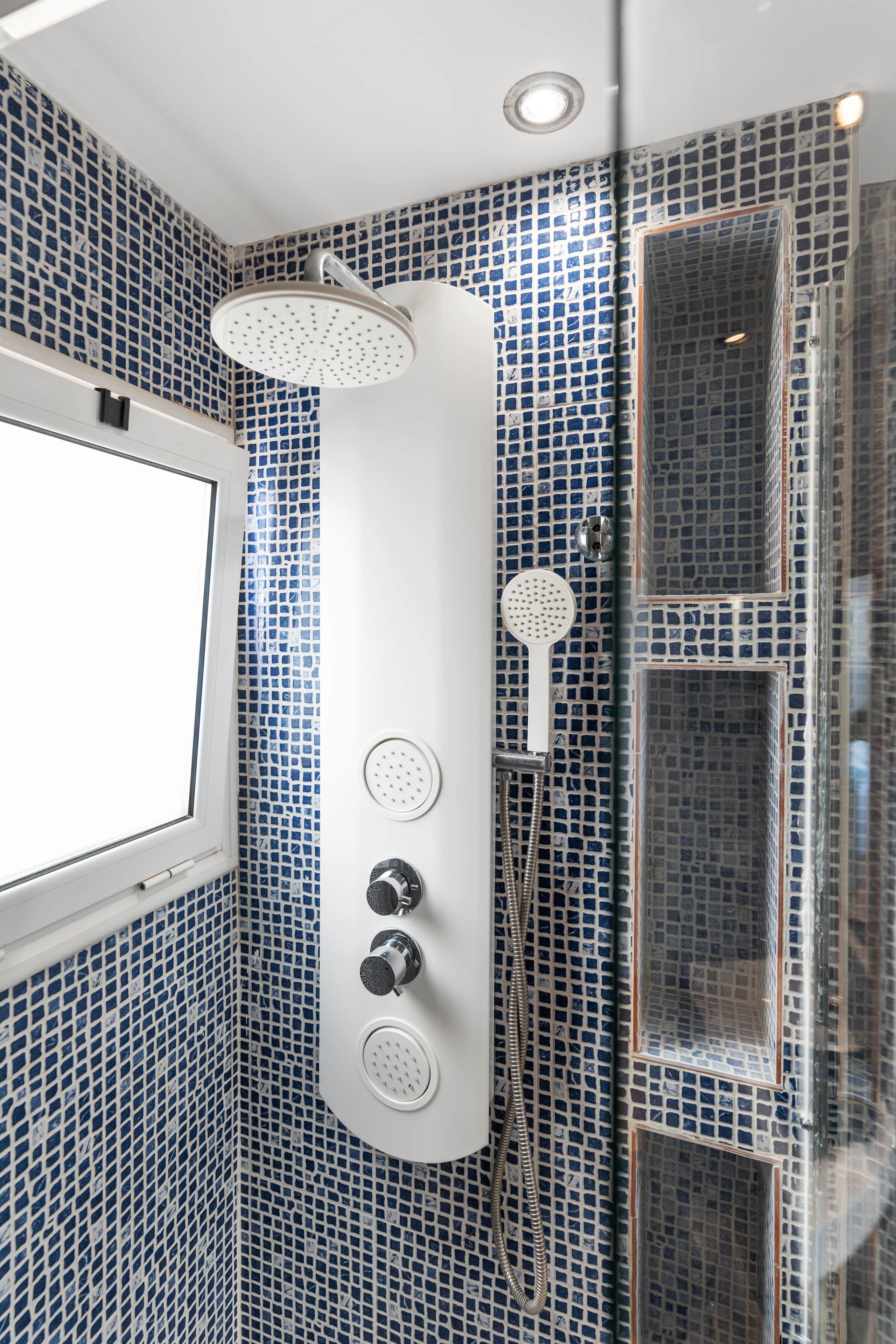 A bathroom with a shower, a handheld showerhead, and a wall-mounted faucet.