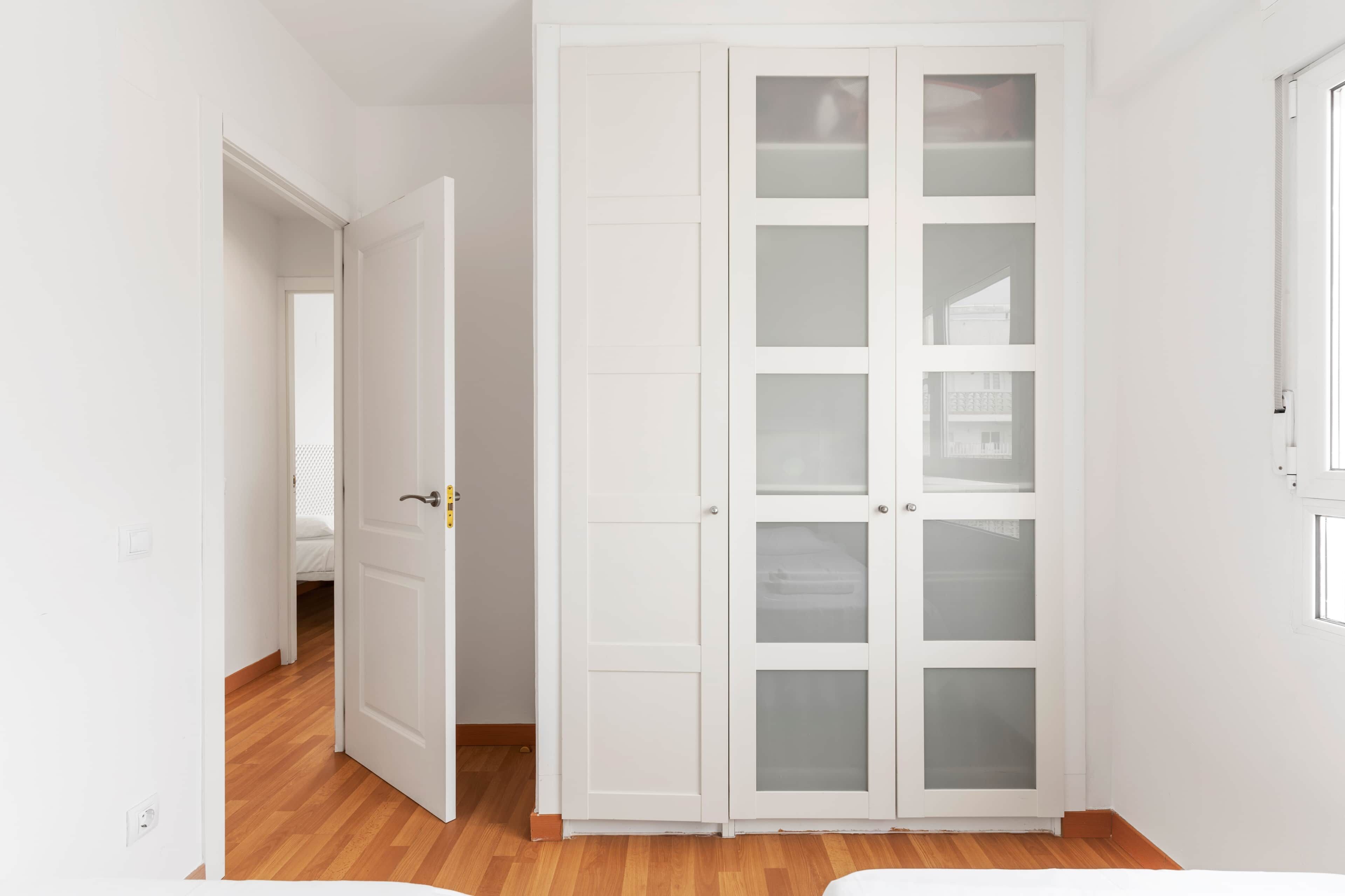 A room with a white wardrobe, a wooden floor, and a door leading to another room.