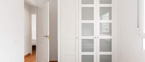 A room with a white wardrobe, a wooden floor, and a door leading to another room.