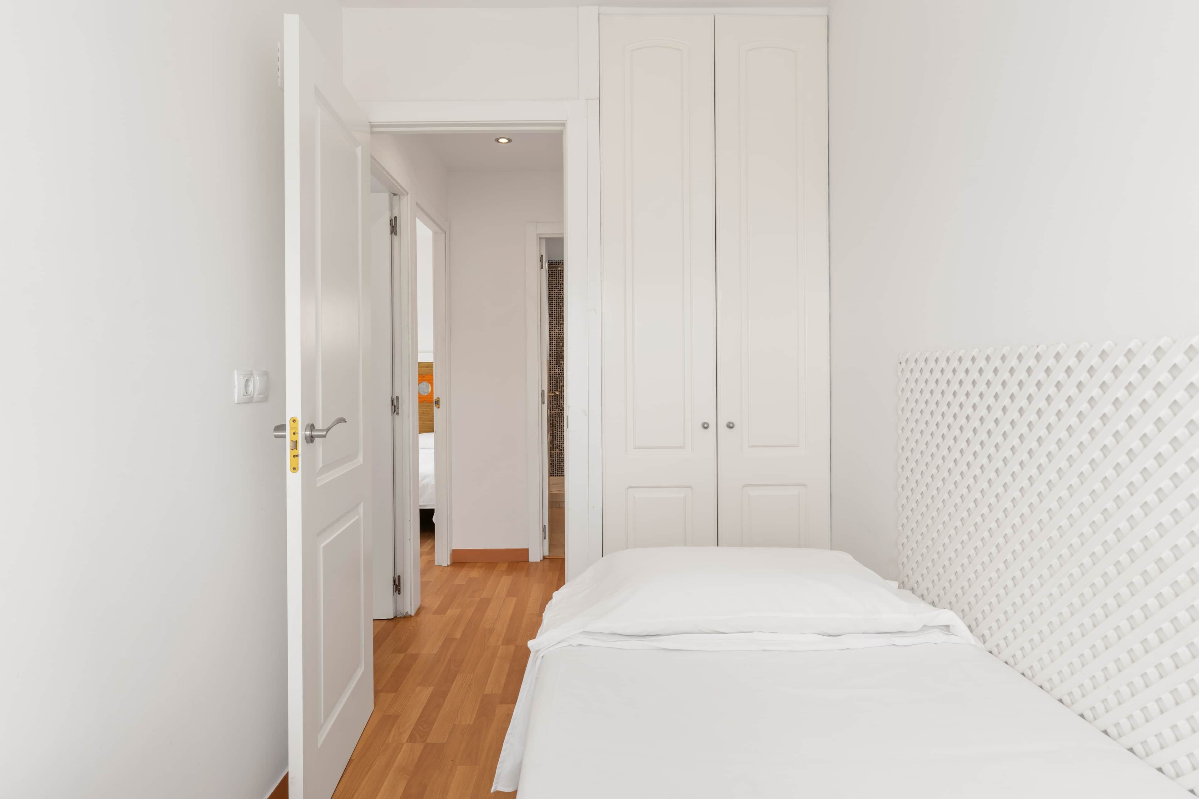A bedroom with a bed, white wardrobe, and a door leading to another room.