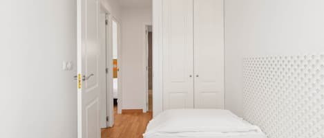 A bedroom with a bed, white wardrobe, and a door leading to another room.