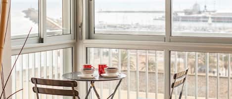 Un balcon avec une table et deux chaises, donnant sur une marina où sont amarrés des bateaux.