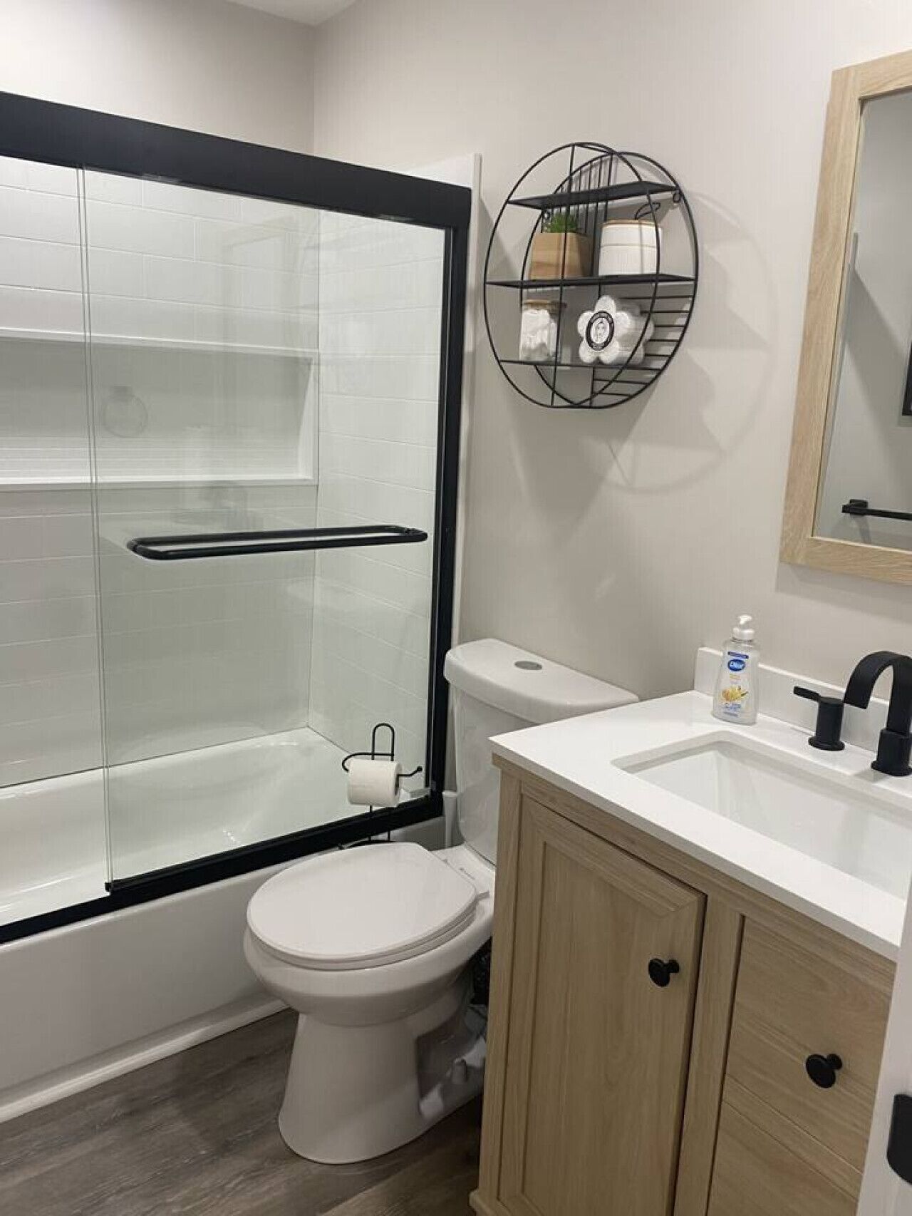 A modern bathroom with a glass shower enclosure, a toilet, a sink with a black faucet, and a wooden cabinet.
