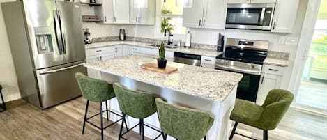Una cocina moderna con una isla central, electrodomésticos de acero inoxidable y taburetes de bar verdes.