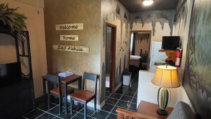 Ein gemütliches Zimmer mit Essbereich, einer Lampe und Wandbildern mit den Schildern 'Welcome Home' und 'Stay Awhile'.