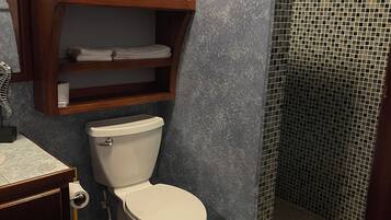 Ein Badezimmer mit Toilette, Ablagefläche mit gefalteten Handtüchern, Dusche mit Mosaikfliesen und dunklem Fliesenboden.